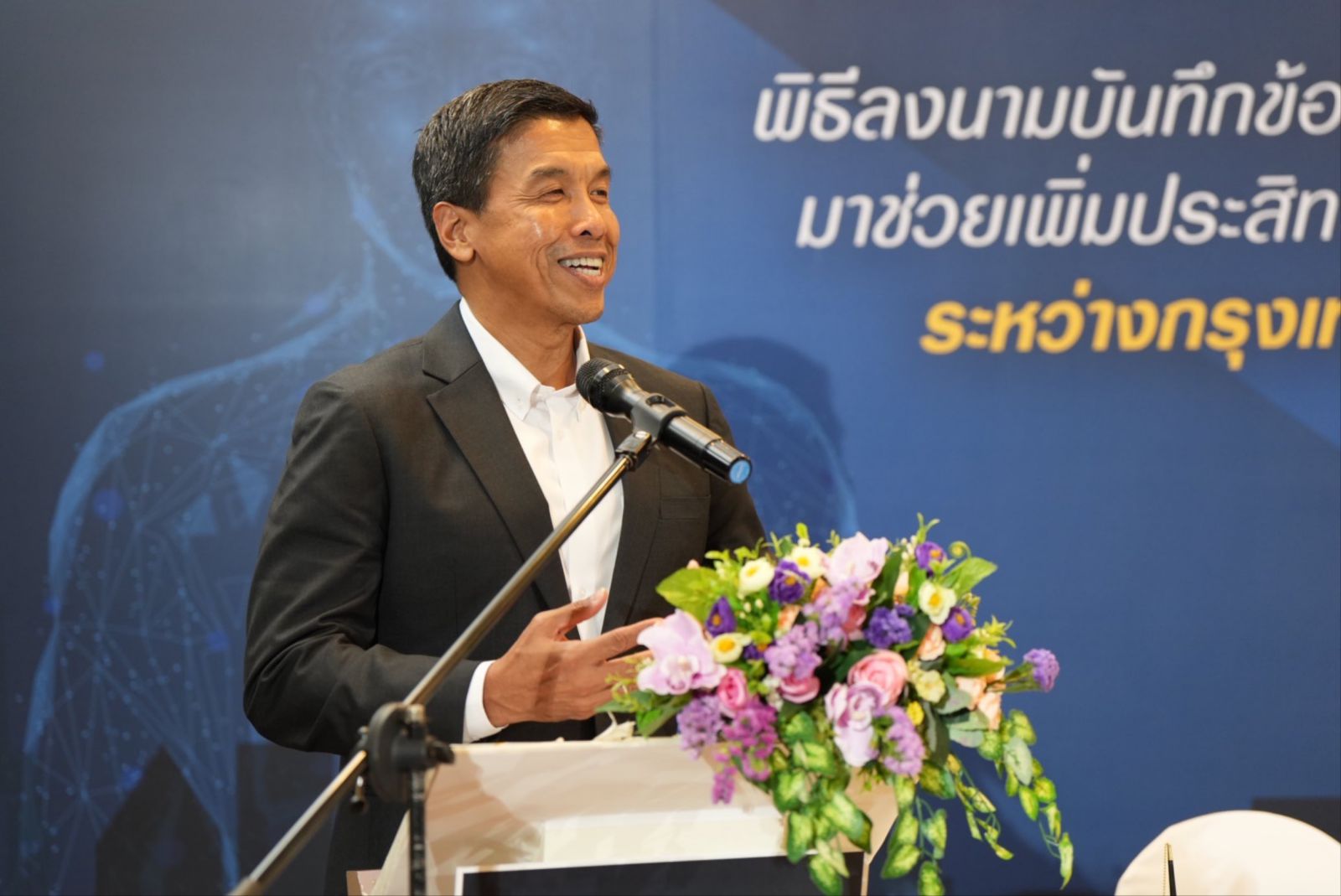 A person standing at a podium with a microphone and flowersDescription automatically generated